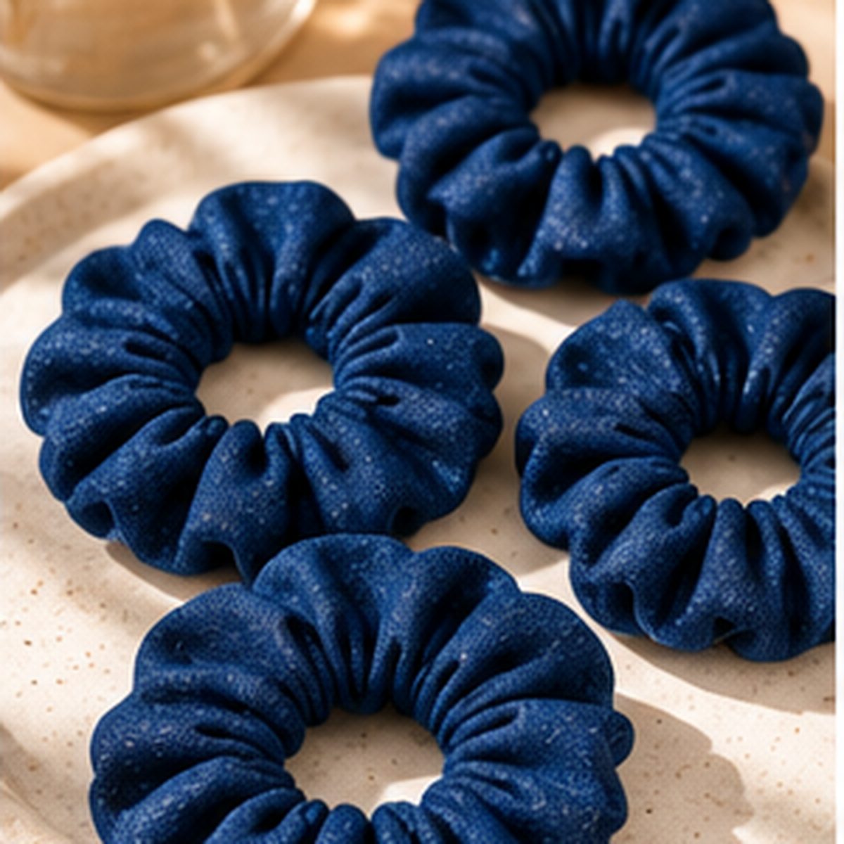 Four dark blue fabric scrunchies arranged on a light beige speckled plate.