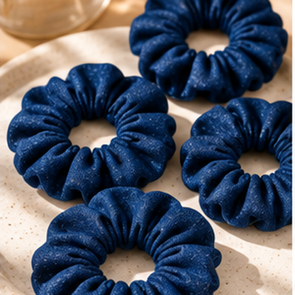 Four dark blue fabric scrunchies arranged on a light beige speckled plate.