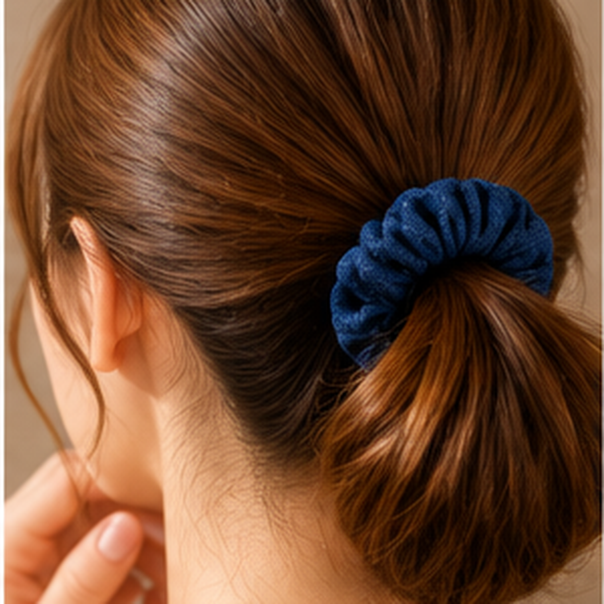 A close-up of a person's hair tied back in a low bun with a textured, ribbed navy blue scrunchie.