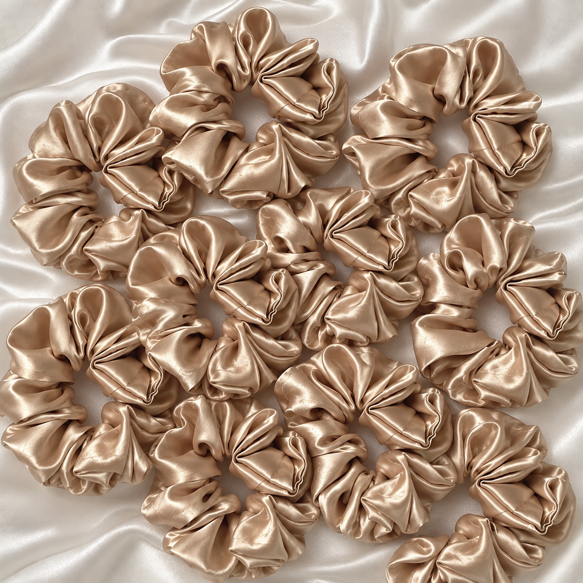 Champagne gold satin hair scrunchies arranged on an ivory satin background